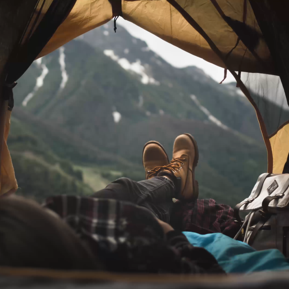 Person entspannt im Zelt mit Blick auf bergige Landschaft