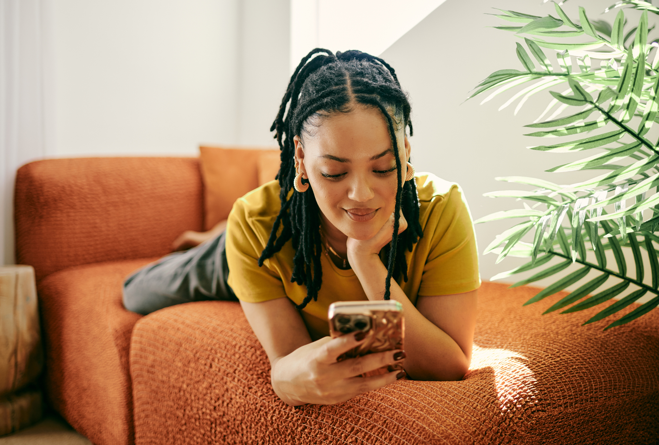 Frau auf einem orangefarbenen Sofa, die auf ihr Telefon schaut.