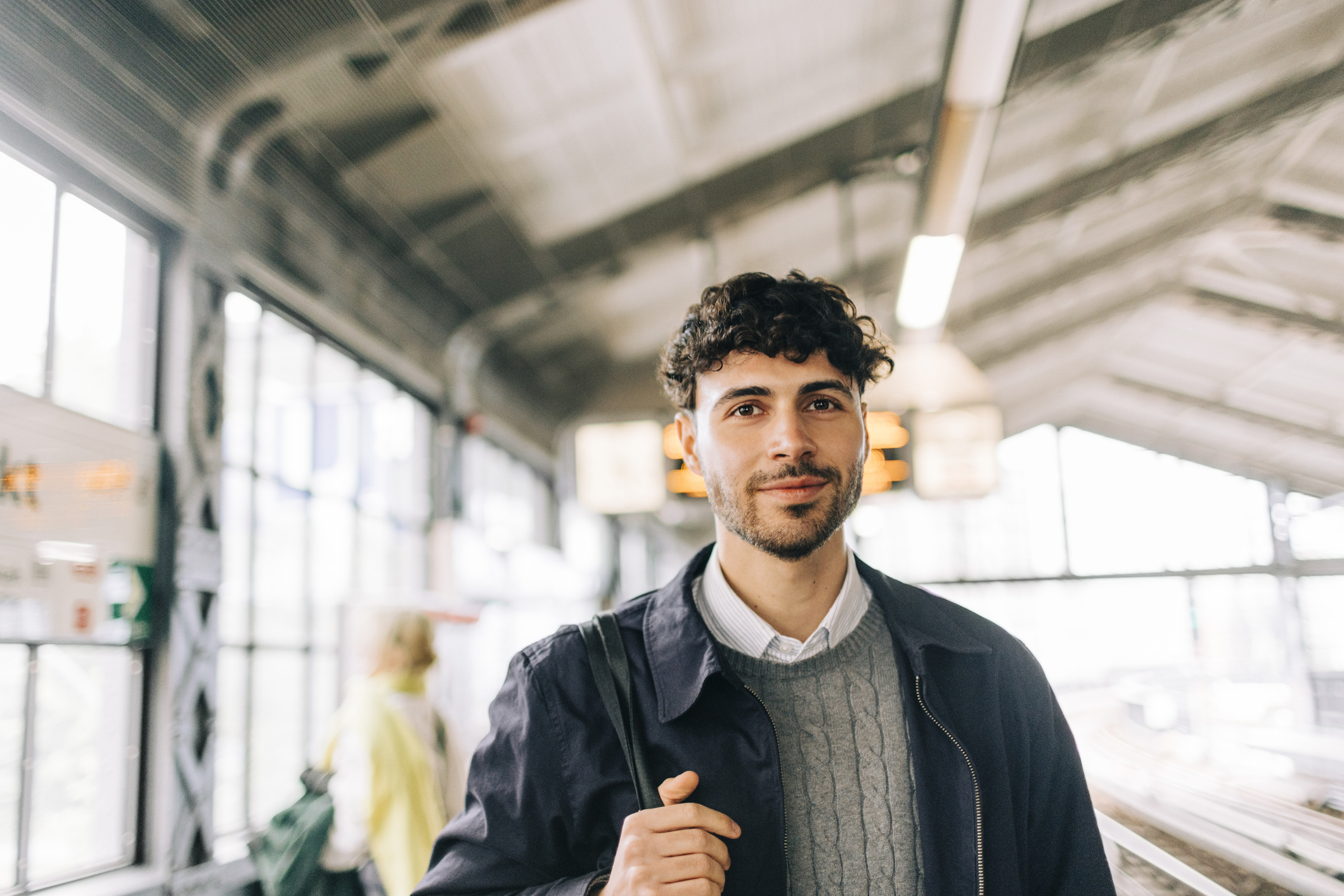Porträt eines lächelnden jungen Geschäftsmanns, der eine Jacke am Bahnhof trägt.