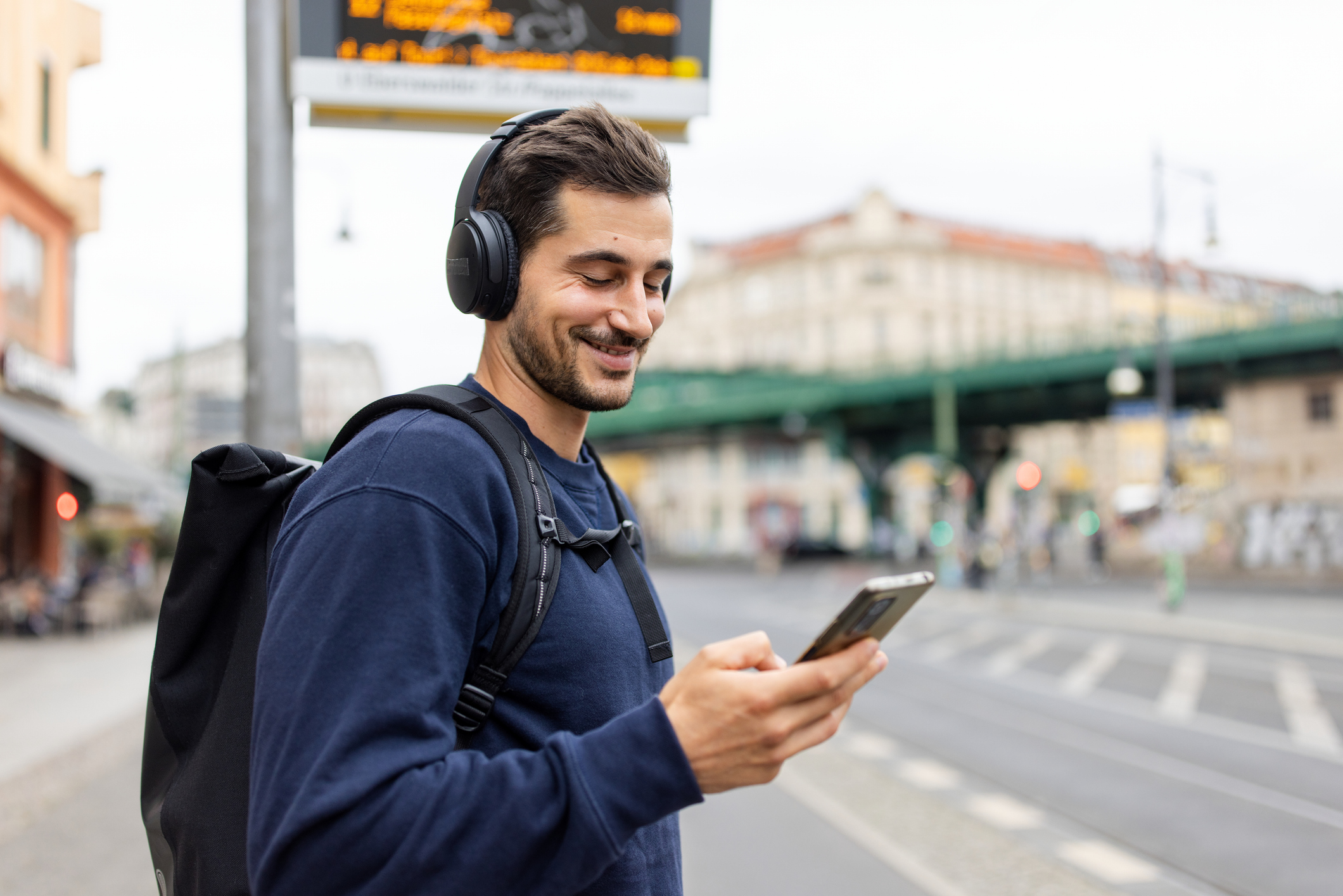 Happy man using smartphone while listening to music in an urban setting, Berlin cityscape.