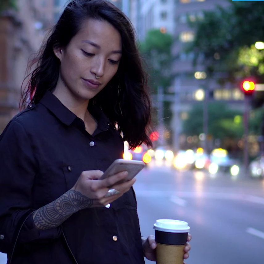 Woman on her phone with a coffee in the street 